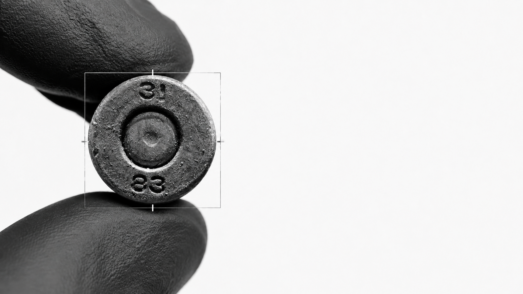 Headstamp exploitation image showing cartridge base markings held between gloved fingertips